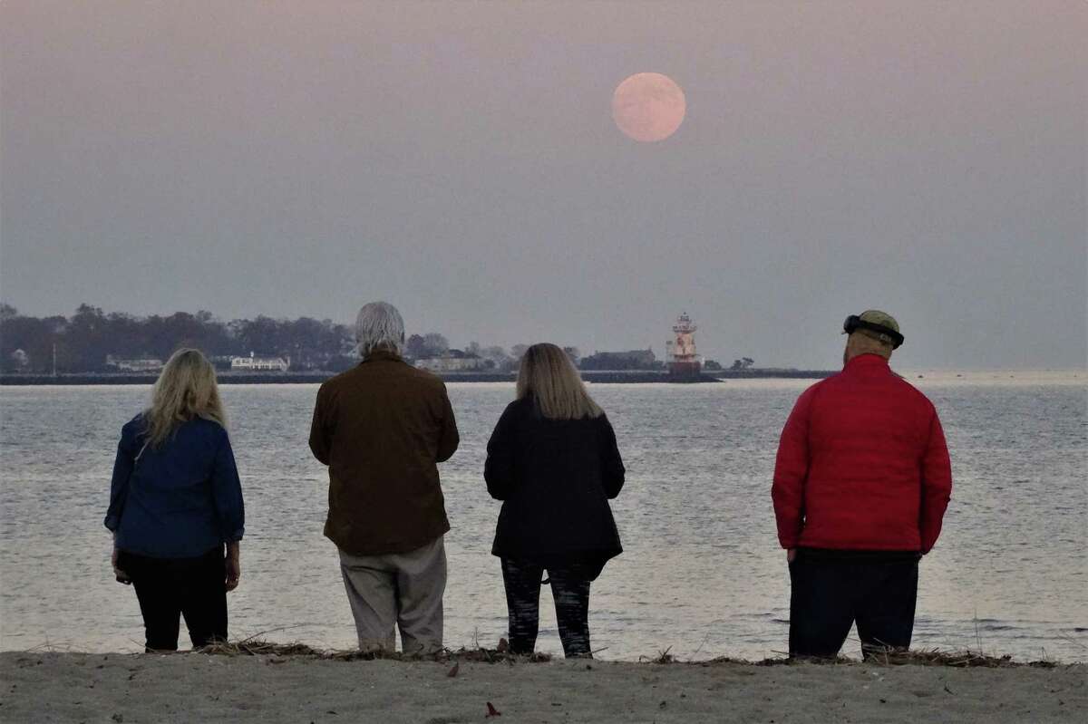 Area residents watch the moon rise over Stamford Harbor Ledge Lighthouse from Greenwich Point in Greenwich, Conn., on Thursday November 18, 2021. Tonight’s full moon is known as the Beaver Moon and will appear full through Saturday morning, according to NASA.