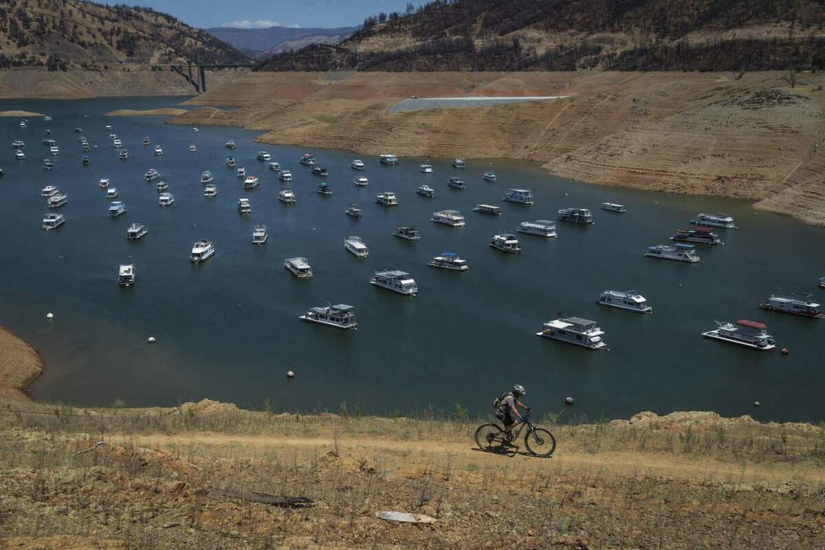 A bicyclist rides on the hillside above houseboats whose owners chose to leave them in the lake, at a water level nearly 200 feet below normal at the Bidwell Canyon Marina at Lake Oroville in June.