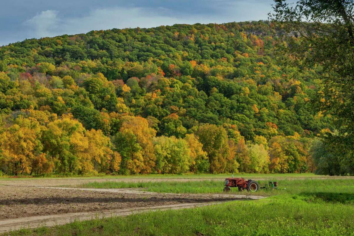 Autumn colors in a variety of trees covering a mountainside above a farm with tractor in the field in Simsbury.