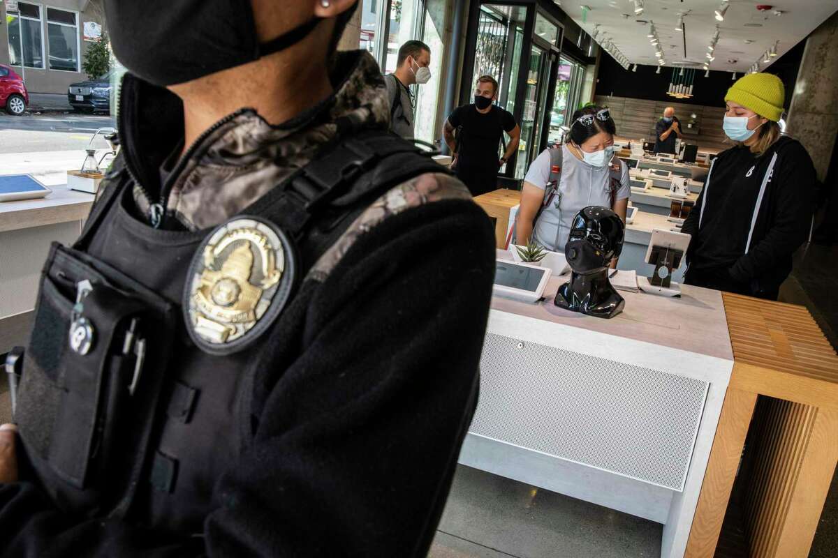 People shop inside b8ta as security guard Ron Legaspi stands by the store’s entrance in the Hayes Valley neighborhood of San Francisco. The company featuring a curated list of consumer electronics, recently reopened its Hayes Valley location six months after an armed robbery forced its temporary closure. The store now utilizes private security around the clock.