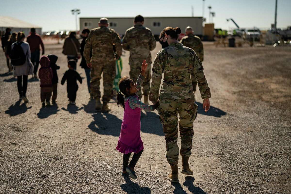 A U.S. military service member holds the hand of an Afghan refugee girl as they walk inside a camp at Holloman Air Force Base in Alamogordo, N.M., on Nov. 4, 2021.