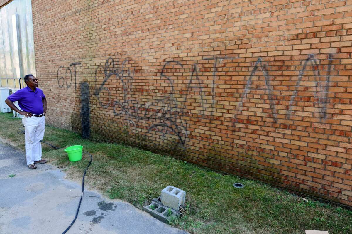 The Rev. Leonard Comithier, Jr., Pastor of Macedonia Baptist Church, looks at graffiti sprayed on an outer wall of the church, as workers attempt to remove it, on Thursday July 12, 2012 in Colonie, NY. (Philip Kamrass / Times Union)