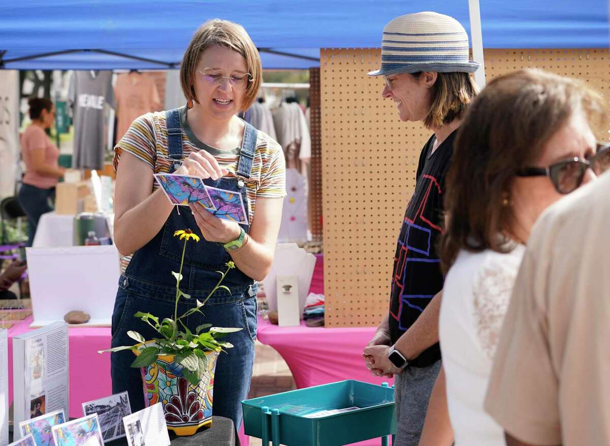 Josie Mitchell, left, talks with Melissa Noble, about East End Postales, a series of English and Spanish postcards that reflects the East End’s natural spaces, during the East End Farmer’s Market Sunday, Nov. 21, 2021 in Houston. She created East End Postales through a grant from a Houston Arts Alliance. The postcards featuring artwork and poetry are printed on seed paper that can be planted.