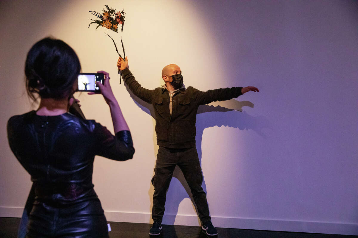 Brooke Li, left, takes a photograph of Phil Koster with one of the interactive pieces of artwork at the "Art of Banksy" unauthorized private collection exhibit at the Palace of Fine Arts in San Francisco on Nov. 21, 2021.