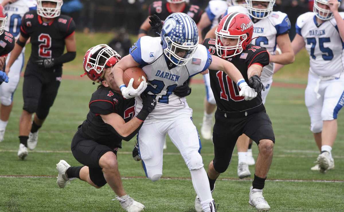 Darien's Jeremiah Stafford (21) runs for some yards while New Canaan's Riley Gardiner (7) and Christopher Bopp (10) attempt to stop him during the Turkey Bowl football game at Dunning Field on Thursday, Nov. 25, 2021.
