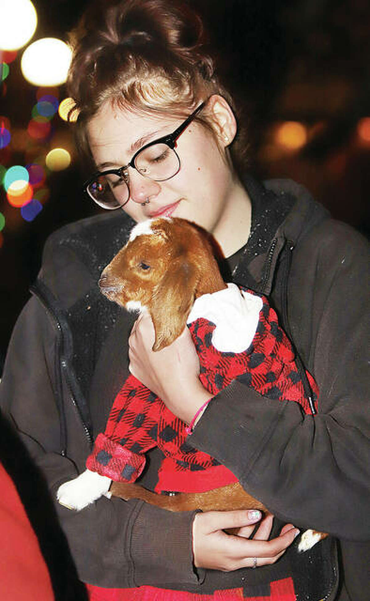Reagan Goewey, from Parker’s Goat Ranch in Fieldon, cuddles a baby goat named Whiskey at the annual tree lighting ceremony Friday night in Alton. 
