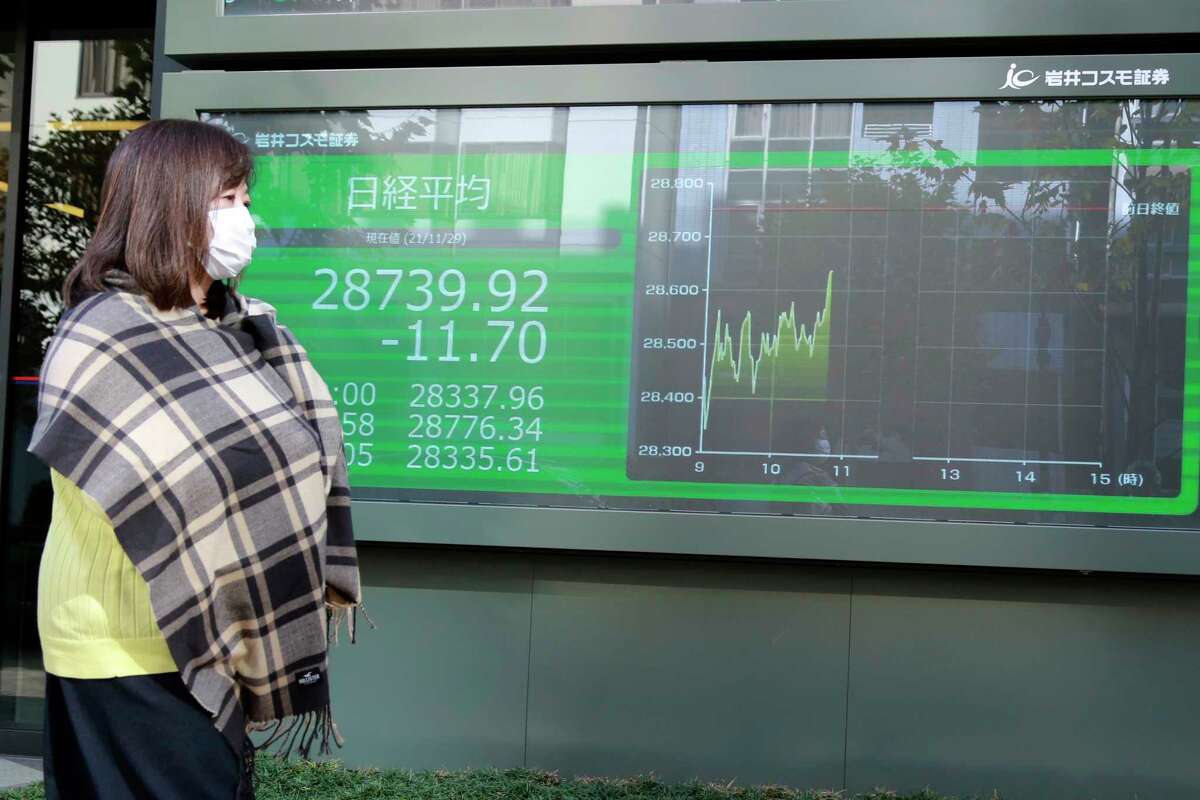 A woman walks by an electronic stock board of a securities firm in Tokyo, Monday, Nov. 29, 2021. Asian stock markets fell further Monday after the omicron variant of the coronavirus was found in more countries and governments imposed travel controls.