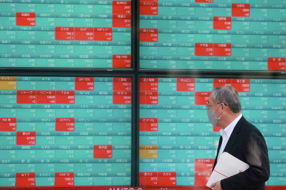 A man walks past an electronic stock board of a securities firm in Tokyo, Monday, Nov. 29, 2021. Asian stock markets fell further Monday after the omicron variant of the coronavirus was found in more countries and governments imposed travel controls.