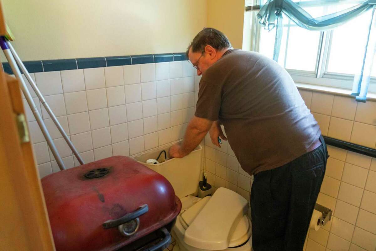 Kent Churchill reaches into the tank of his broken toilet to show how he flushes it because of its broken handle, Monday, Nov. 29, 2021, at the Acres Homes Gardens apartments in Houston. A group of tenants living in the 15-unit apartment building have organized with the Houston Tenants Union and have delivered a demand letter to their landlord asking for timely repairs, pest control and an end to alleged threats and harassment made by management. Management has agreed to meet with tenants.