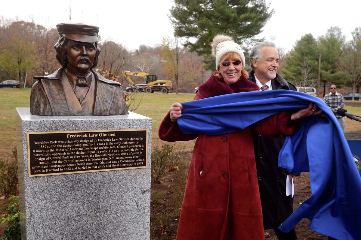 Artist and sculptor Louise Wiley unveils her bust of Frederick Law Olmsted during a ceremony in Beardsley Park, in Bridgeport, Conn. Nov. 30, 2021. Olmsted designed the park in the 1880s and the new bust of his likeness was dedicated to mark the upcoming 200th anniversary of his birth in 1822. Wiley is seen here with State DOT Commissioner Joseph Giulietti, who led the ceremony.