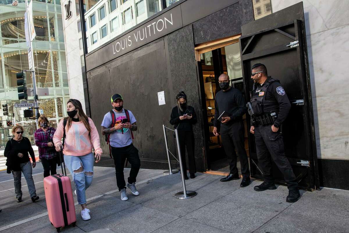 People stroll past a barricaded Louis Vuitton store on Union Square.