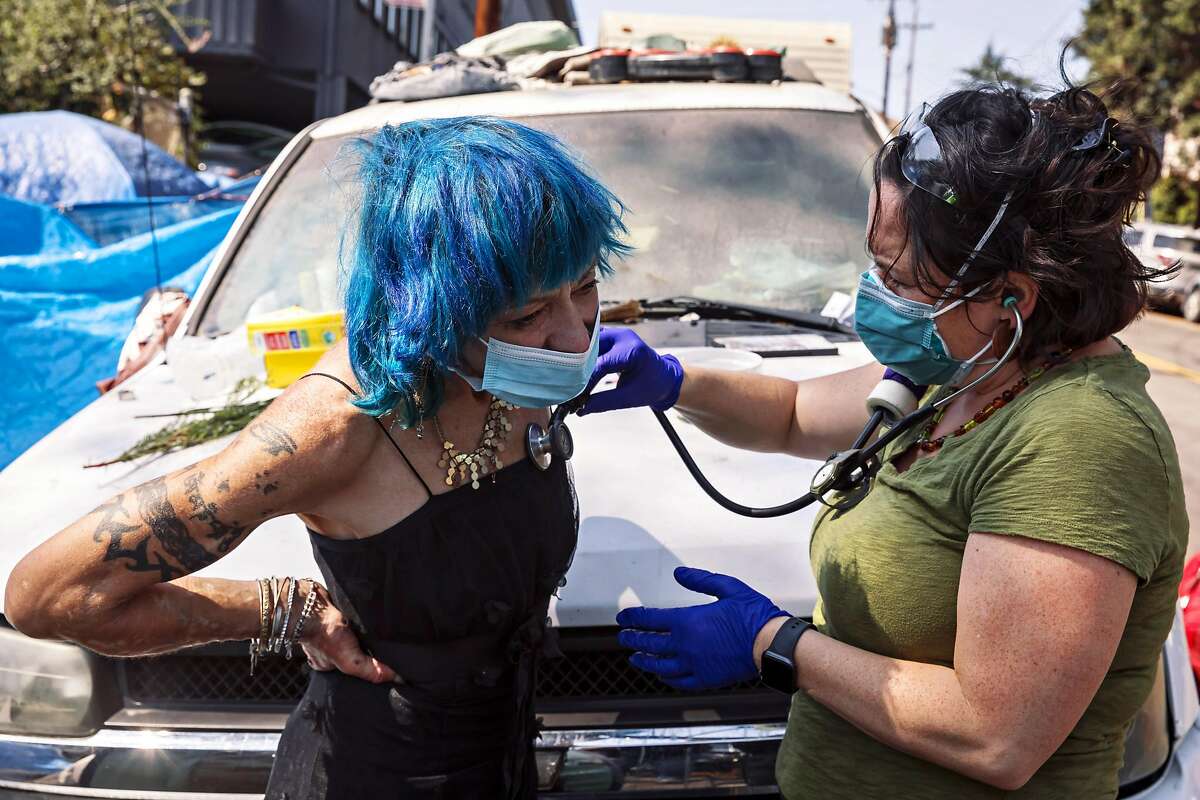 Gwyn Teninty, left, gets checked out by Christine Salera, a nurse practitioner with Trust Street Medicine, Lifelong Medical Care, after she became sick and was worried about a Covid-19 infection at her homeless camp in Oakland, Calif., on Wednesday, September 8, 2021.