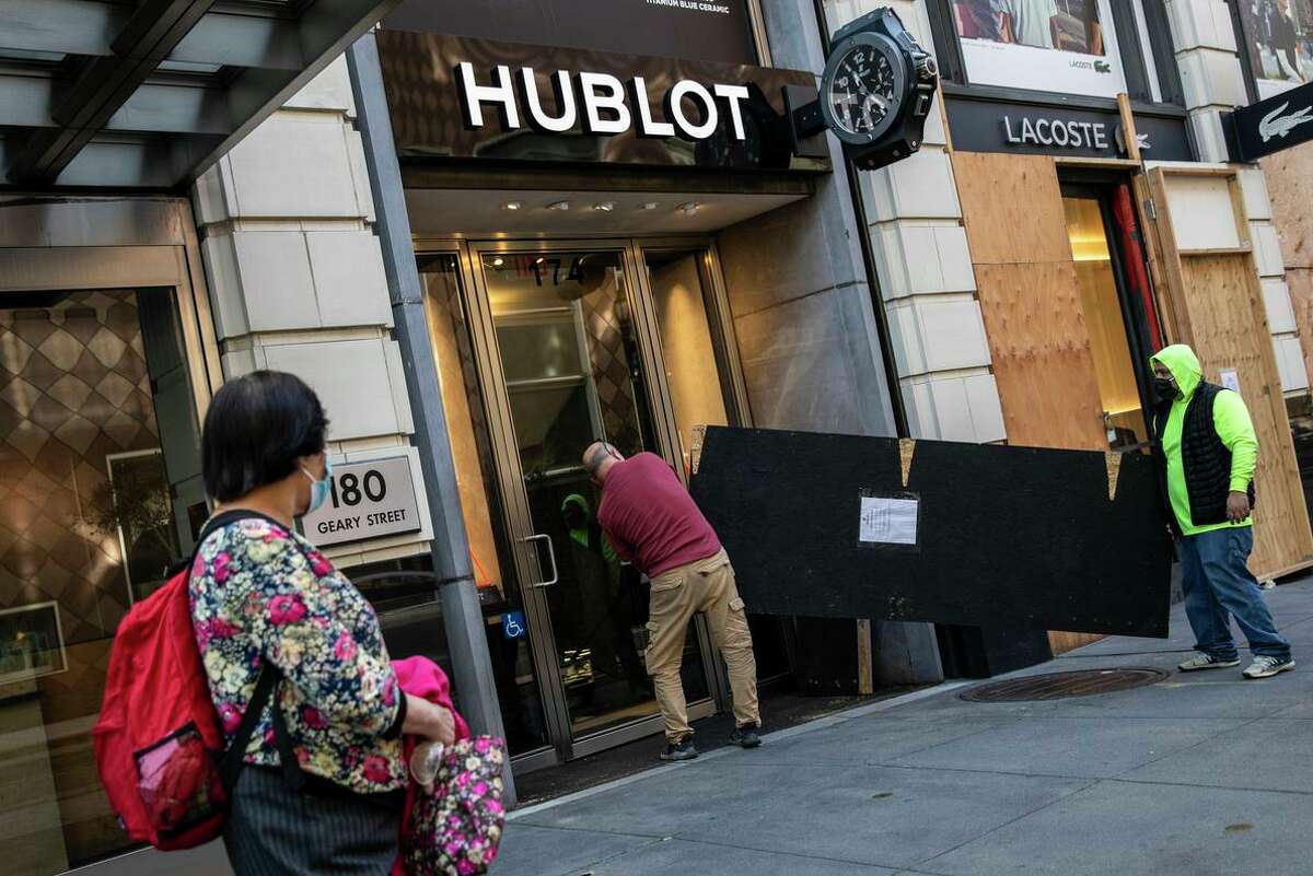 Workers carry a board to reinforce the door at Hublot near Union Square after robbers swarmed stores. Supporters of the city are rallying to help.