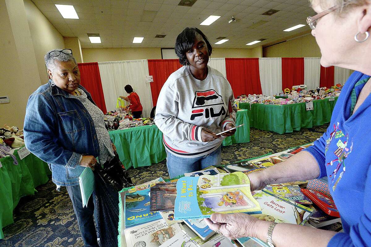 Volunteer Claris Collins (right) helps Marian Harris find books for her children and one for herself while she shops fo her gifts with Emilie West (left) amid the tables filled with toys and other gifts at the annual distribution of the EJ Empty Stocking Fund gifts to families in need at the Compro Event Center. Photo taken Wednesday, December 5, 2018 Kim Brent/The Enterprise