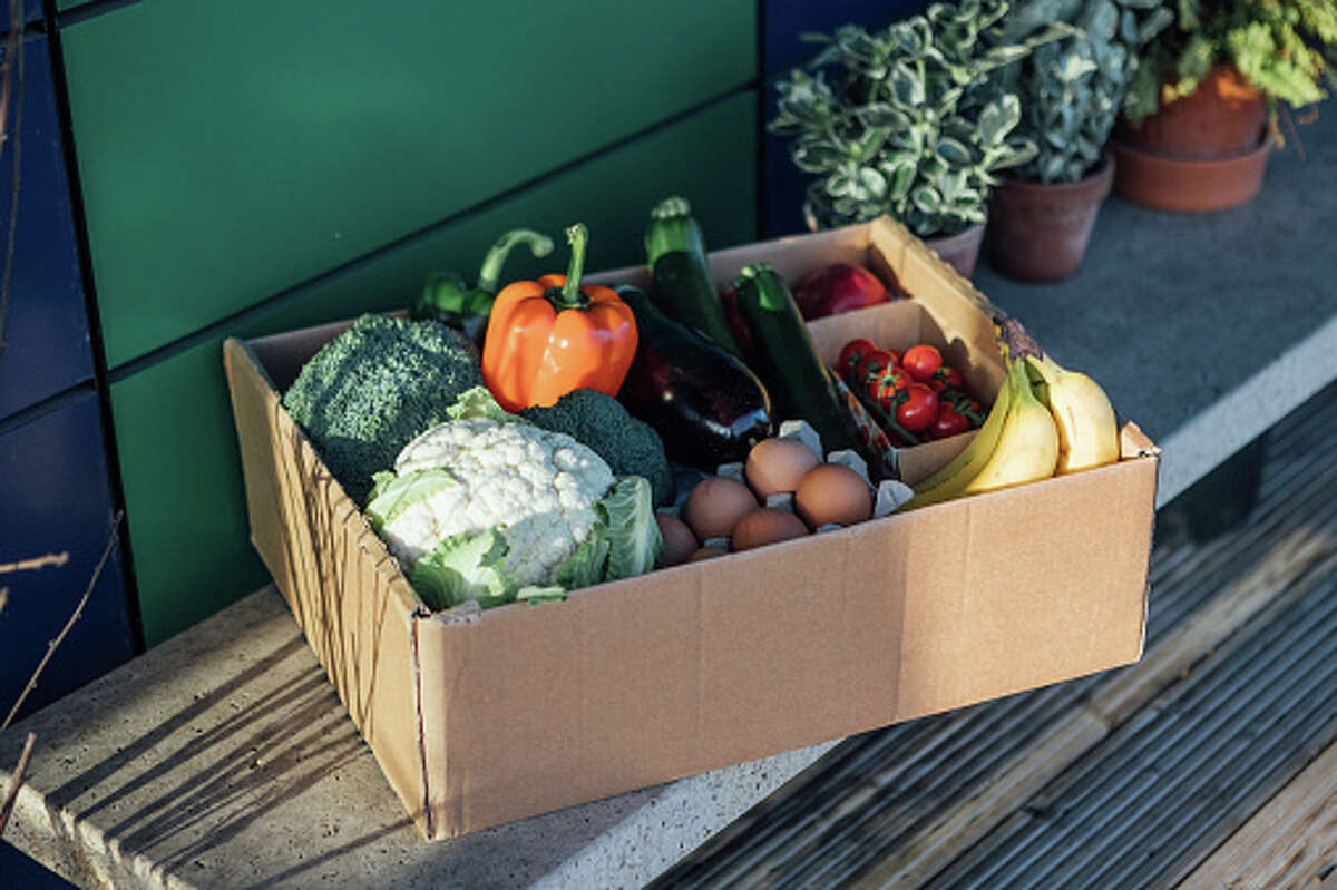 A delivery box filled with fresh organic vegetables and fruits on the front yard.