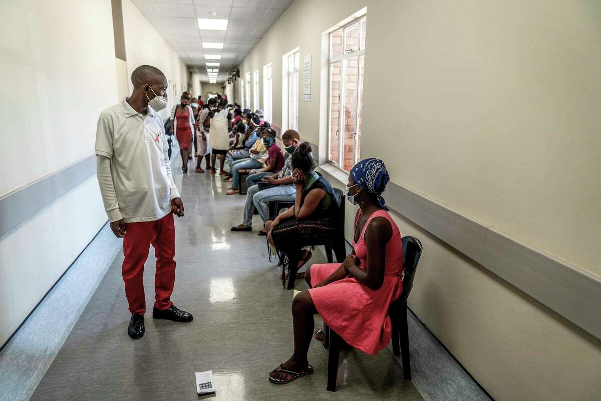 A hospital worker ensures people practice social distancing as they wait in line to get vaccinated against COVID-19 at the Lenasia South Hospital near Johannesburg, South Africa. The omicron variant, first found in South Africa, has now been identified in San Francisco.