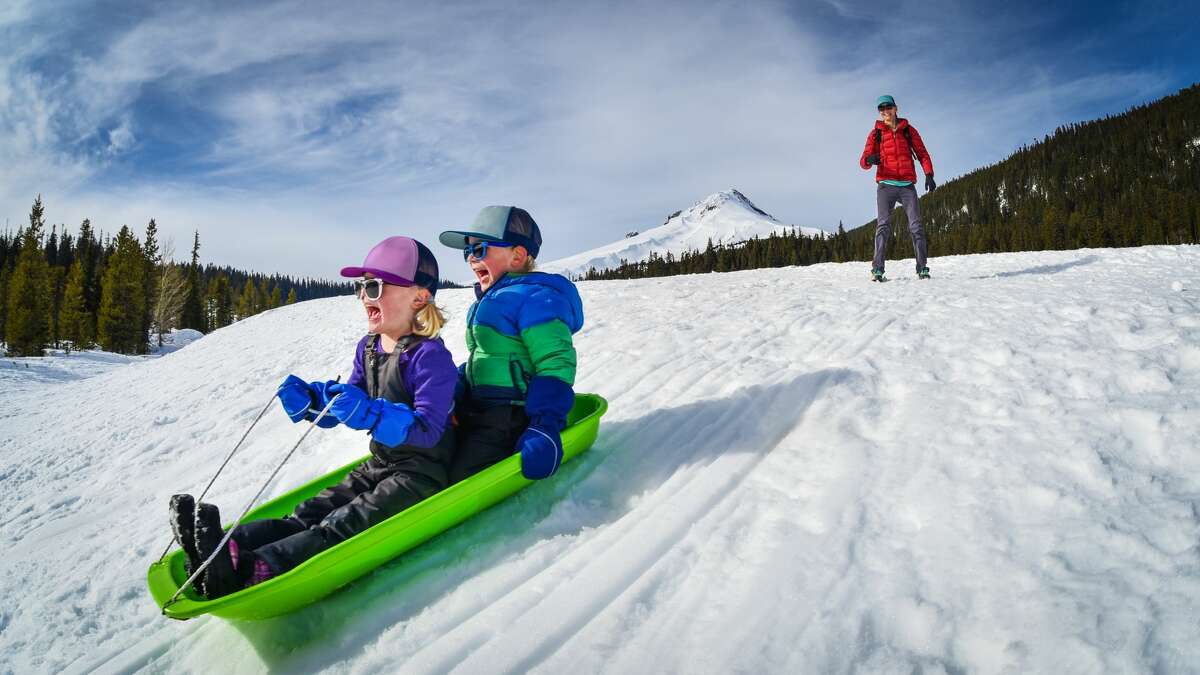 Two kids race down a snowy hill at Mount Hood, Oregon.