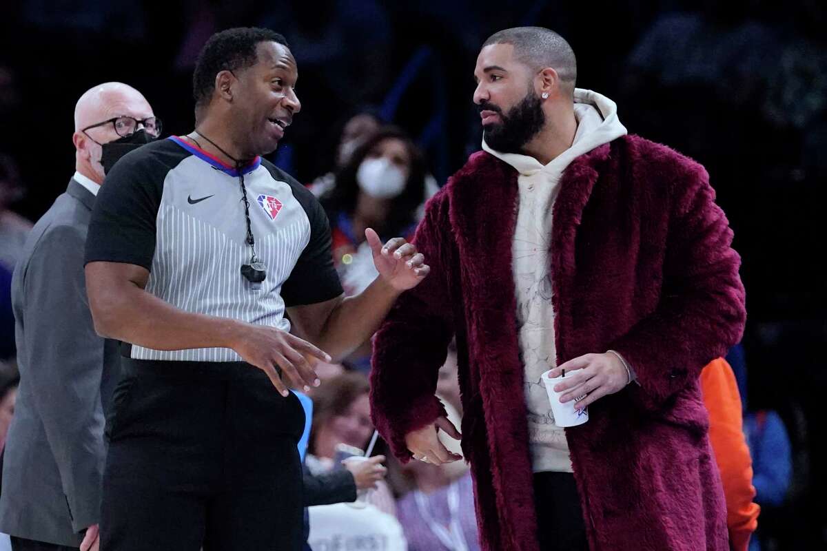 Referee Mitchell Ervin, left, talks with rapper Drake, right, during the second half of an NBA basketball game between the Houston Rockets and the Oklahoma City Thunder, Wednesday, Dec. 1, 2021, in Oklahoma City. (AP Photo/Sue Ogrocki)