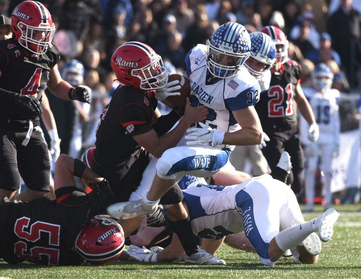 Darien’s Tighe Cummiskey (32) is tackled by New Canaan’s Barrett Schmitz (2) and Stephen Luccarelli (56) during a football game on Thursday, November 25, 2021 in New Canaan, Conn.