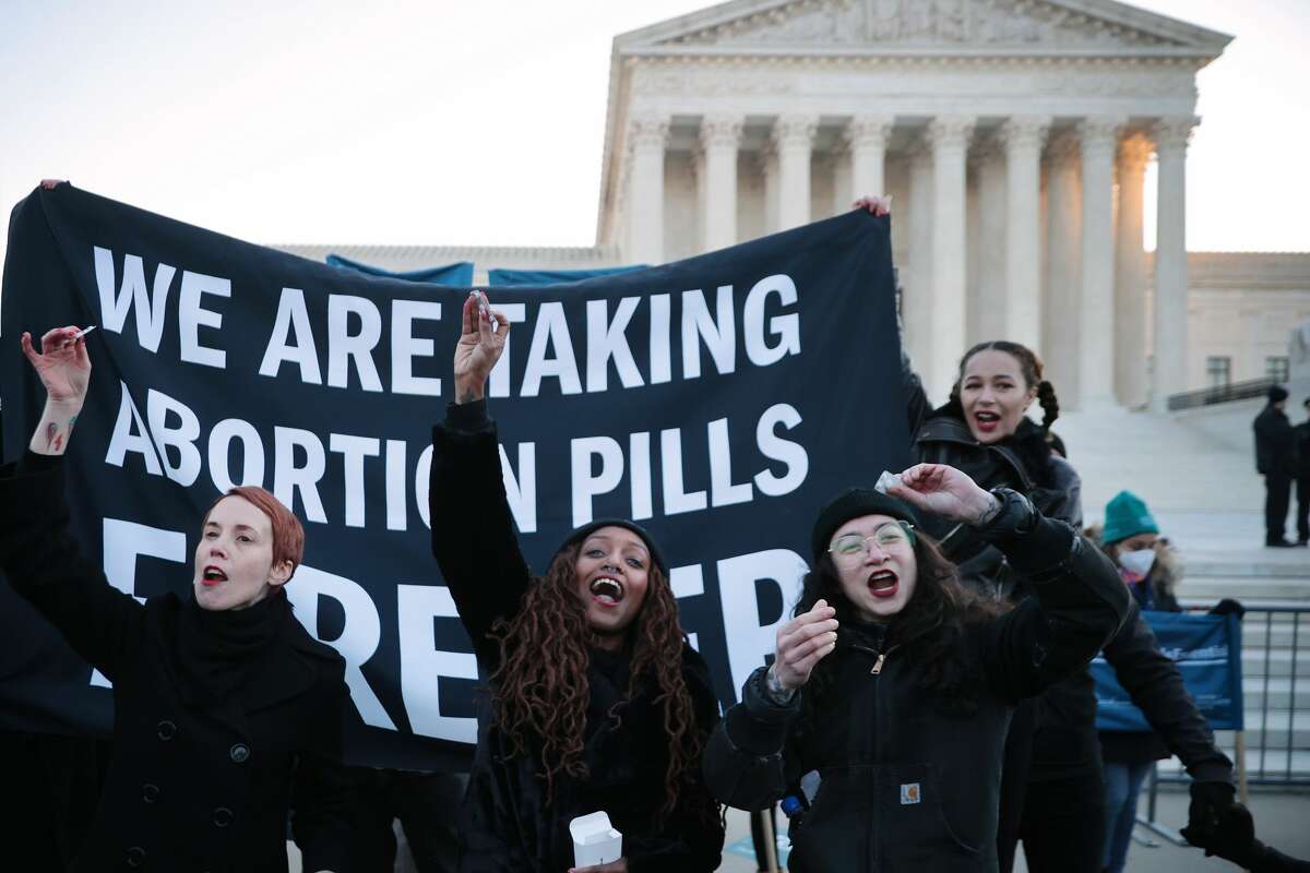 Lila Bonow, Alana Edmondson and Aiyana Knauer prepare to take abortion pill while demonstrating in front of the U.S. Supreme Court as the justices hear hear arguments in Dobbs v. Jackson Women's Health, a case about a Mississippi law that bans most abortions after 15 weeks, on December 01, 2021 in Washington, DC.