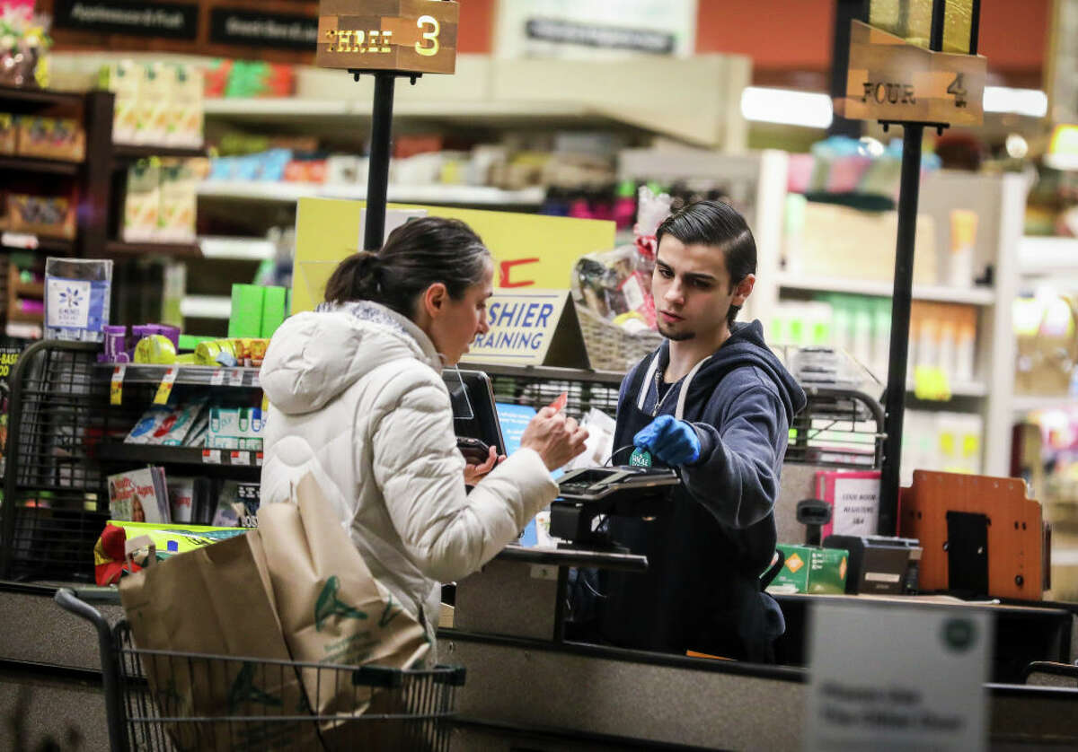 A cashier wears gloves while scanning the groceries of a customer at a grocery store. For workers, anxiety and stress have increased as supermarkets become more crowded.