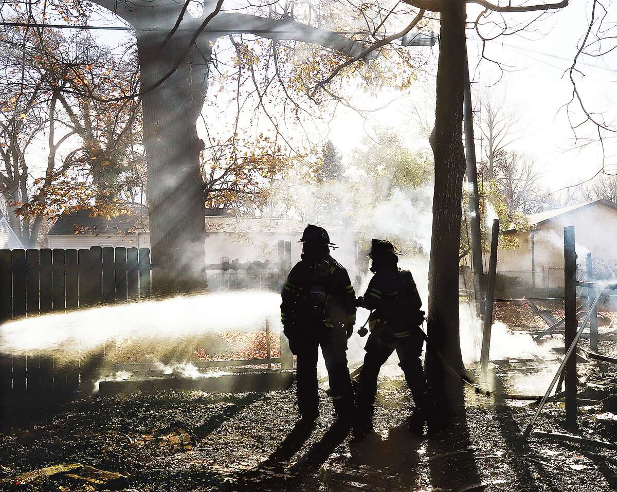 John Badman|The Telegraph Firefighters are silhouetted by the sun through the smoke as they finish extinguishing a Thursday afternoon fire that spread to grass and trees in the area behind a home on Horn Avenue.