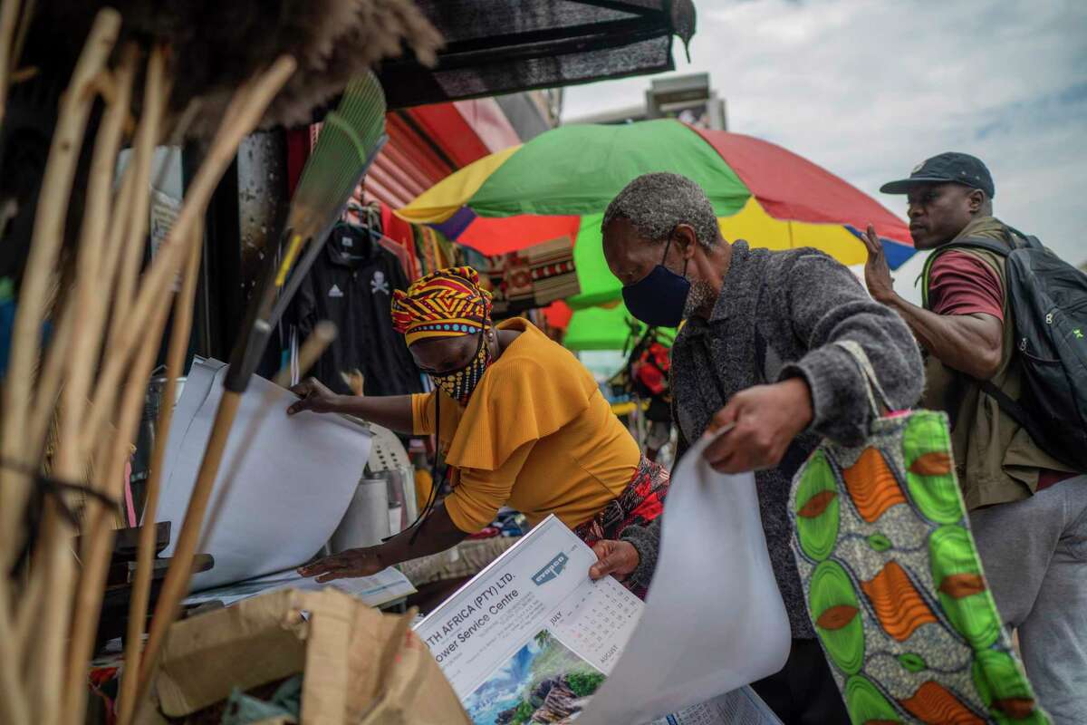 A masked couple sorts through goods at an outdoor market near the Baragwanath taxi rank in Soweto, South Africa, Thursday Dec. 2, 2021. South Africa launched an accelerated vaccination campaign to combat a dramatic rise in confirmed cases of COVID-19 a week after the omicron variant was detected in the country.