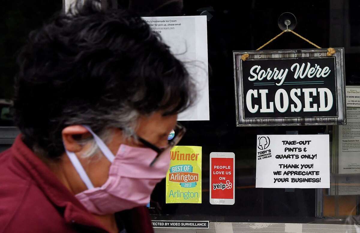 (FILES) In this file photo taken on May 5, 2020 a woman wearing a face mask walks past a sign in the window of a food store announcing that the business is closed during a shelter in place lockdown order during an outbreak of COVID-19 coronavirus in Arlington, Virginia. - The coronavirus arrived in the US early this year, followed by deaths, business shutdowns and layoffs, rendering a previously healthy economy unrecognizable. Data from the government and private surveys has shown that the economic damage is deep and may take years to recover from, but on Friday, a new Labor Department survey is expected to show unemployment spiking, perhaps to as high as 20 percent, a number few living Americans have ever seen before. Ahead of the report's release, AFP spoke to three people about how the virus has changed the course of their lives in the world's largest economy. (Photo by Olivier DOULIERY / AFP) (Photo by OLIVIER DOULIERY/AFP via Getty Images)