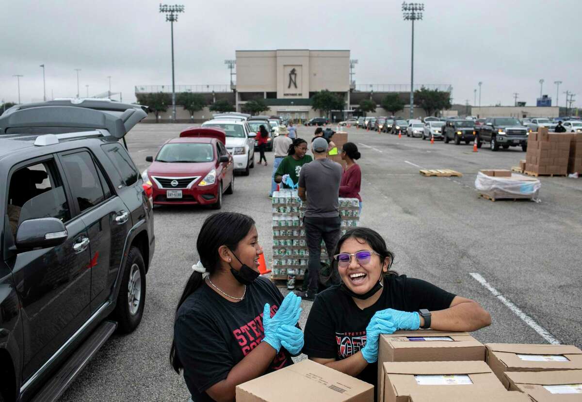 John Paul Stevens High School students Annalisa Juarez-Perales, 16, and Ilana Mendiola, 16, share a laugh while volunteering at a San Antonio Food Bank distribution at Gustafson Stadium on Friday.