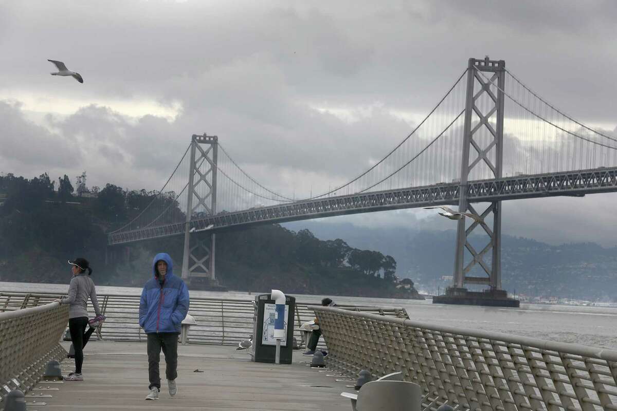 Saturday’s cloudy skies and cold temperatures will give way to a warmer Sunday and chance of rain next week. This file photo shows another cloudy day in San Francisco on Mar. 5 2019, with a view of the Bay Bridge seen from Pier 14 on the Embarcadero.