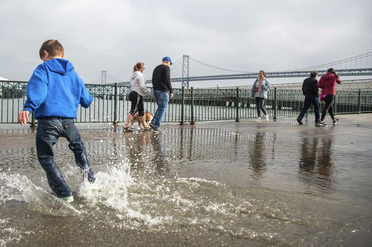 People pass by puddles of water left behind by the king tide that swelled over the Embarcadero pier in San Francisco, California on Saturday, December 4, 2021. More king tides were expected along San Francisco’s coastline starting New Year’s Day.