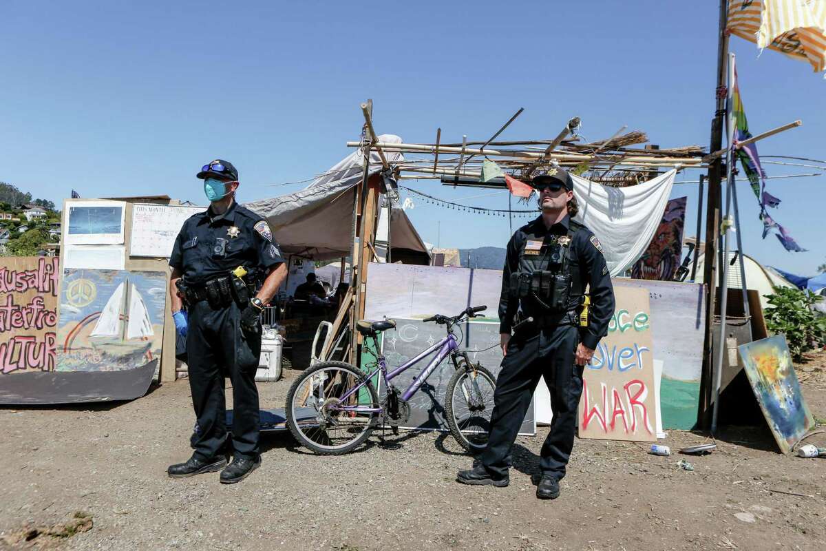 Officers stand in front of an encampment during a protest of the forced move of Camp Cormorant from Dunphy Park to Marinship Park on Tuesday, June 29, 2021 in Sausalito, Calif. A different encampment in Sausalito became the scene of a different conflict, when police arrested a journalist documenting homelessness on Nov. 29, 2021.