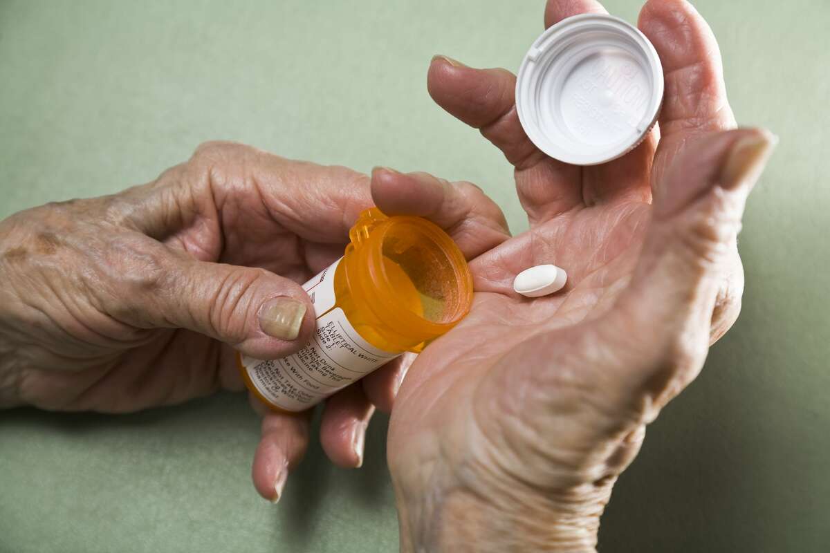 A file image of a senior citizen with arthritis holding prescription medicine pill bottle