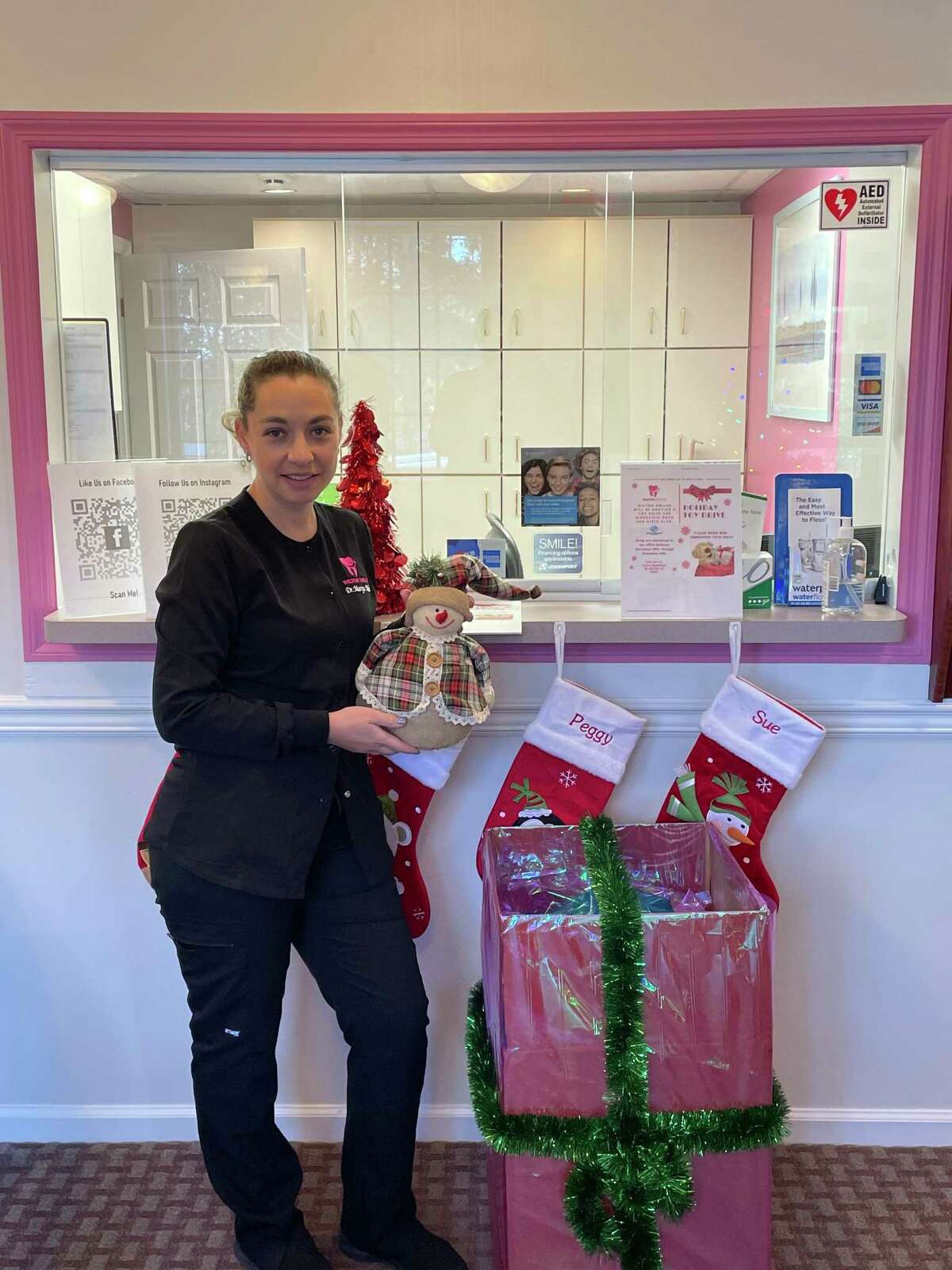 Dr. Mariya Malin alongside the holiday toy drive dropoff at her business, Wilton Smiles, on Old Ridgefield Road. She has organized the drive to collect toys for the Ridgefield Boys and Girls Club.