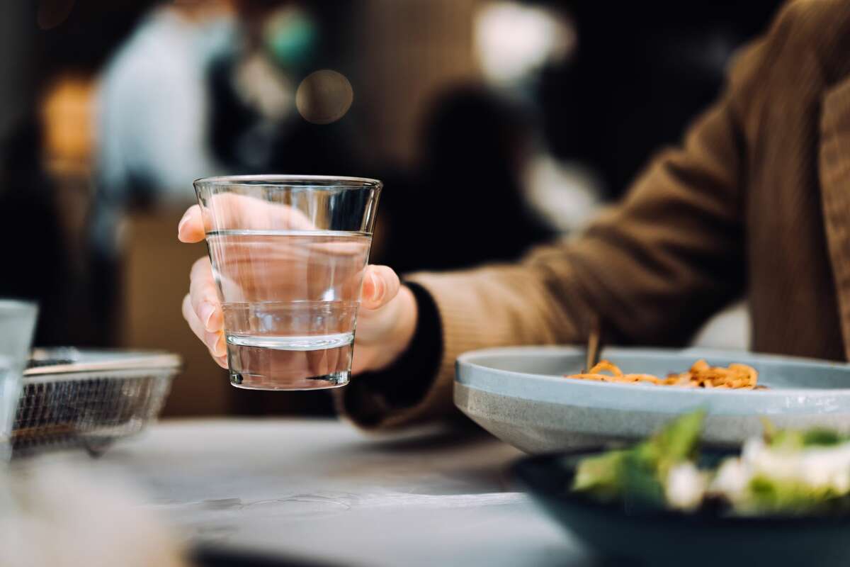 A close-up of a young woman drinking a glass of water while having a meal in a restaurant.