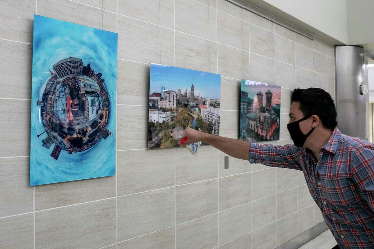 Artist Gabriel Zeckua points to large prints of his drone photography on display near the TSA check point in Terminal A at San Antonio International Airport.