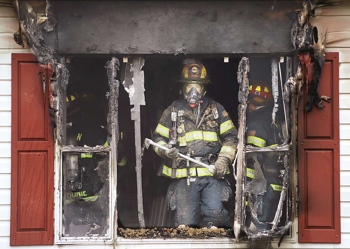 John Badman|The Telegraph An Alton firefighters stands near the window in the rear of a mobile home Tuesday in the 300 block of Aladdin Avenue in Alton following a fire that extensively damaged the home. A couple and a young child managed to escape the fire.