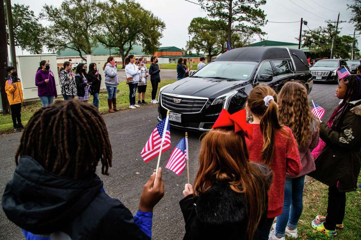 East Chambers Elementary School students wave flags as a hearse carrying the remains of Seaman 2nd Class Charles L. Saunders passes en route to the cemetery on Tuesday, Dec. 7, 2021, in Winnie. About 100 elementary school students stood on the edge of the road to honor the legacy of Saunders 80 years after he died in the attack on Pearl Harbor.