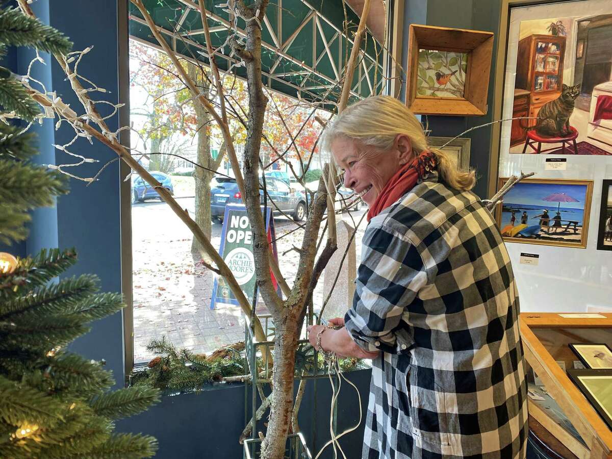 Anda Weyherof the Branford Garden Club helps putting up a holiday display in the front window at the BACA Gallery before the pop-up show.