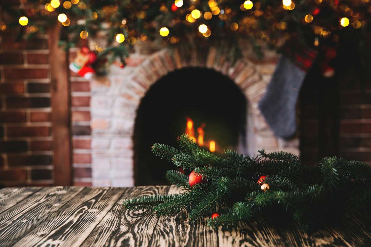 A file image of a Christmas tree branch on a wooden table against the background of a fireplace. 