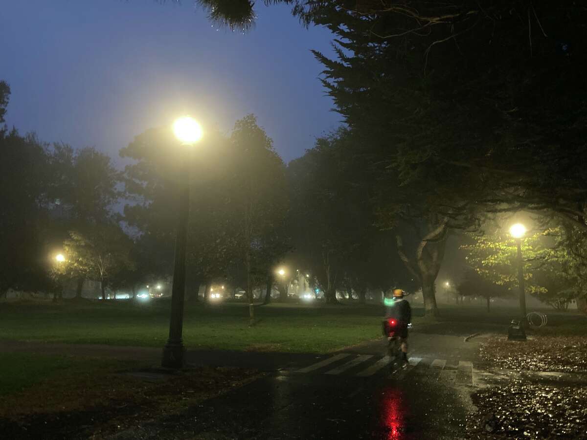 Streetlights and bike lights glow in early morning fog on a bike path in a park in San Francisco.