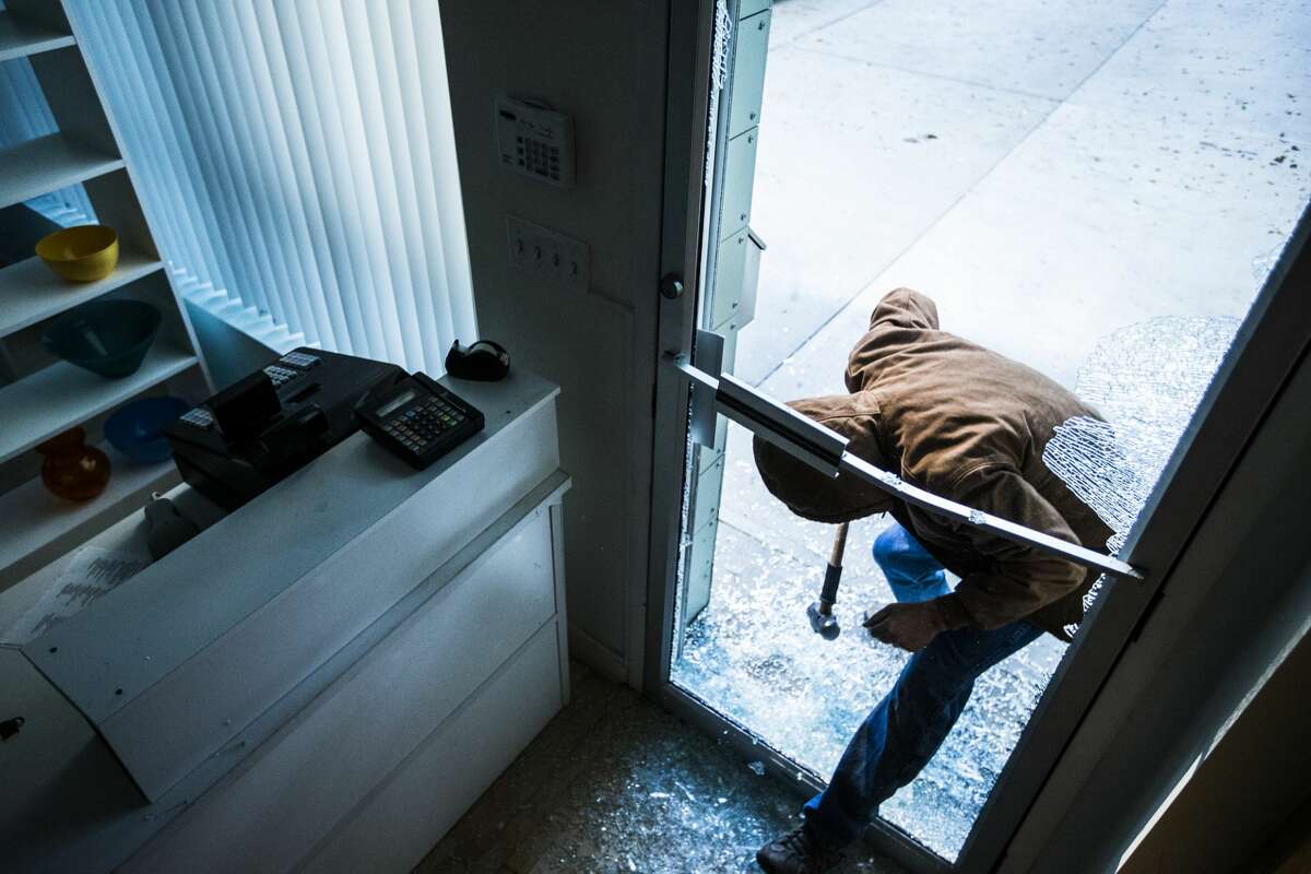 This file images shows a robber using a sledgehammer to break the glass of a retail store.