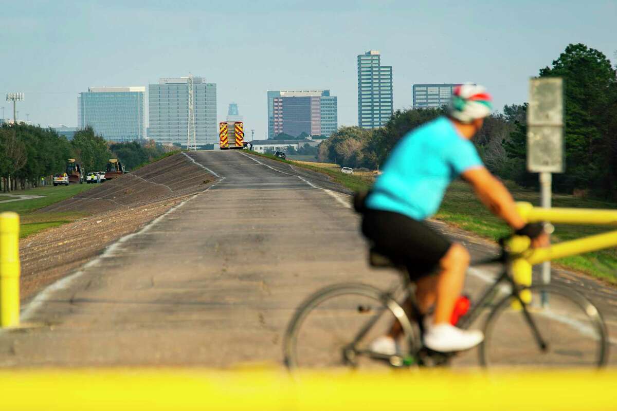 A cyclist passes over the end of Barker Dam near the site where fire and police are responding to a reported small plane crash in the reservoir that killed two people, according to law enforcement, Thursday, Dec. 9, 2021, in Houston.