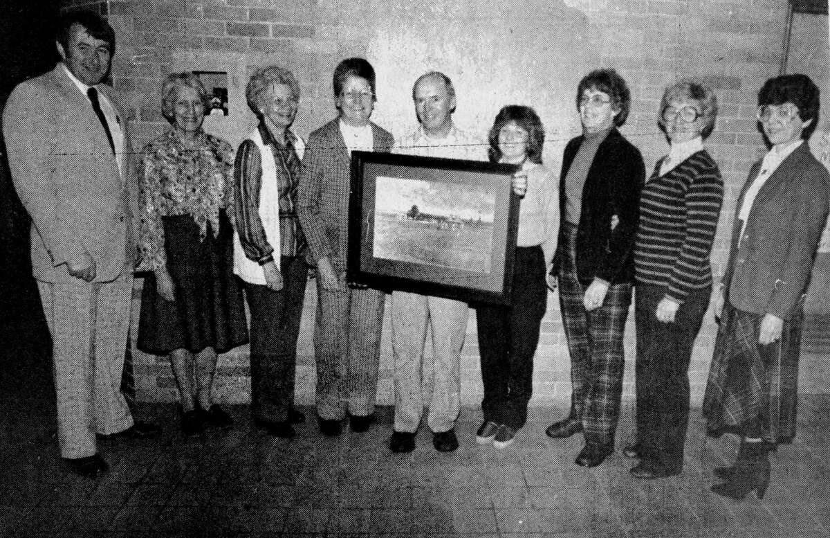 Former Lincoln School Principal Al Anderson (center), now a teacher at North Elementary, was honored yesterday by former Lincoln School staff members with several gifts commemorate his 22 years of service as principal at Lincoln. Standing with Anderson are (from left) Jim Sibley, Marge Johnson, Helen Henry, Sally Berglund, Carol Krolczyk, Pat Williams, Mary Mikolusky and Margaret Laurrsen. Anderson is holding a picture he received from the group. The photo was published in the News Advocate on Dec. 11, 1981.