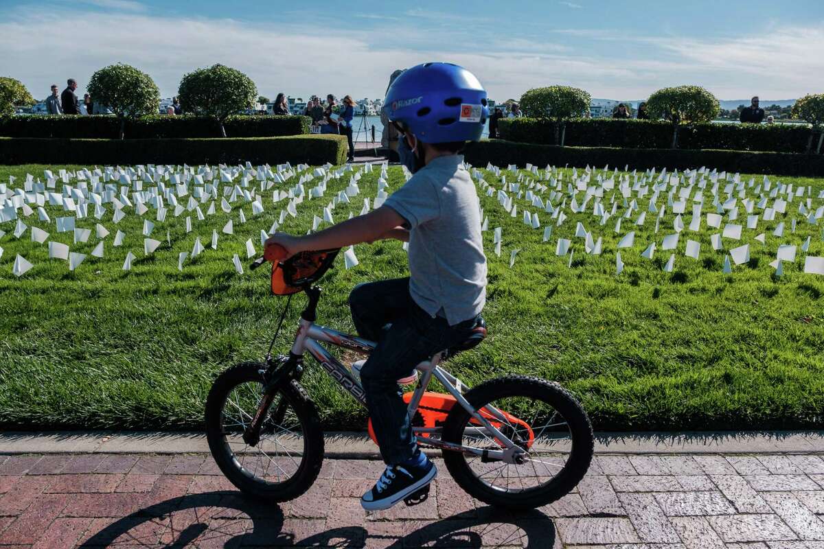 A child rides past small white flags Nov. 7 that are part of an exhibit in Leo Ryan Park titled “In America: Remember,” which gives people a chance to reflect on residents of San Mateo, Calif., who died from COVID-19.