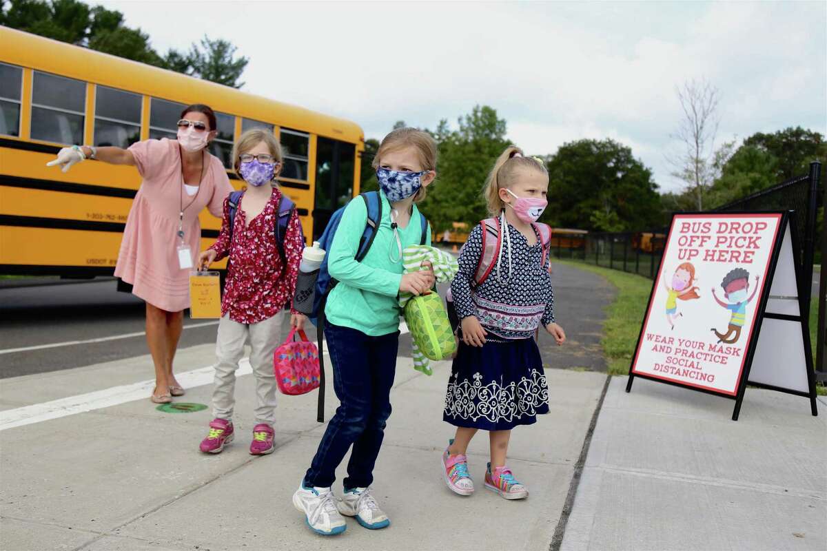 Paraprofessional Mary Jarboe helps guide students from the bus for their first day of in-person classes at Miller-Driscoll on Sept. 8, 2020, in Wilton, Conn.