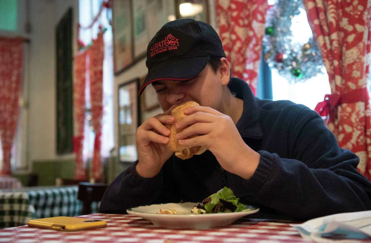 William Mancini, 16, takes a bite out of a chicken sandwich before his shift at Hattie's Restaurant on Friday, Dec. 10, 2021 in Saratoga Springs, N.Y. In the new initiative Miss Hattie's Homework Hour, teen staff can come straight to Hattie’s from school, punch in an hour before their shift, work on homework, and be fed.