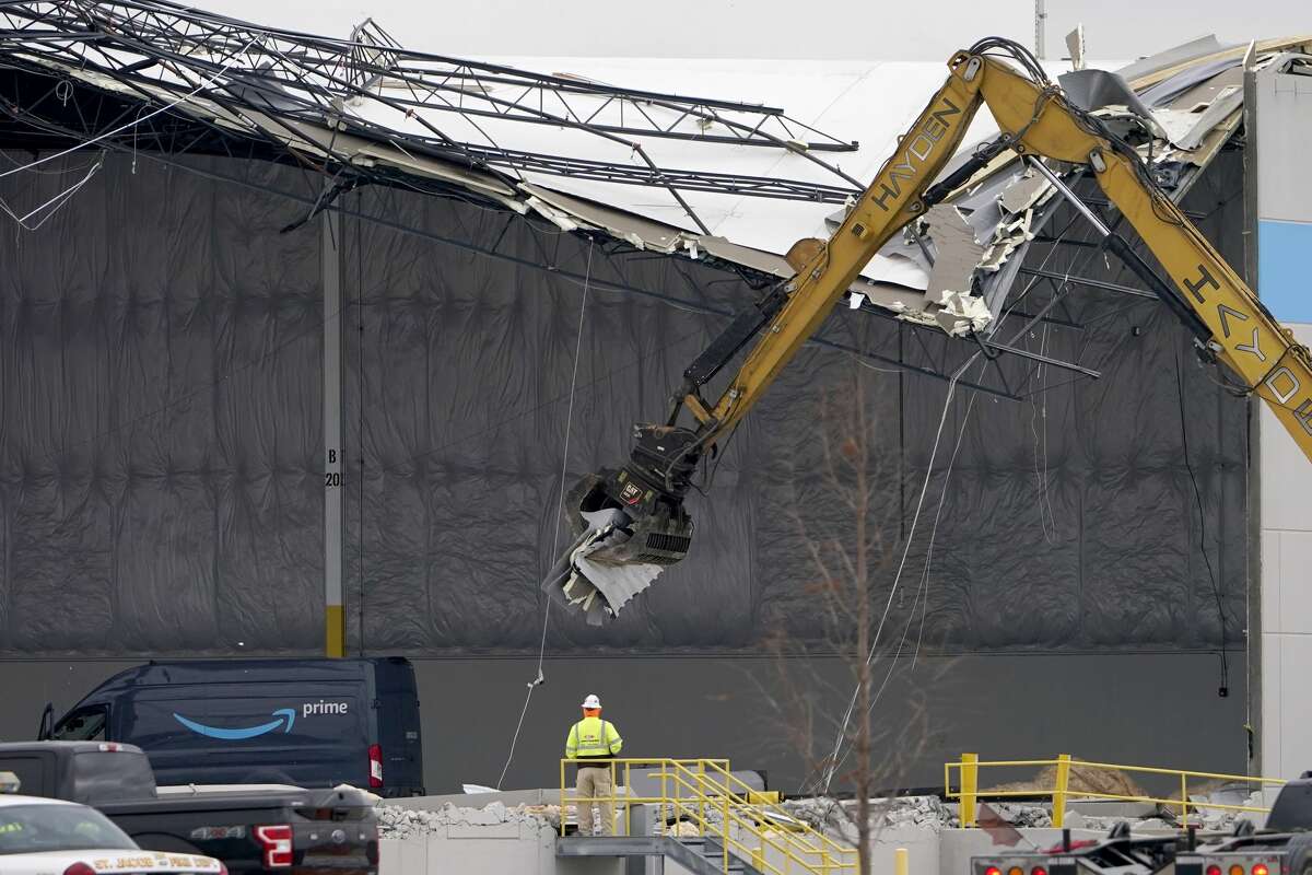 Workers use equipment to remove a section of roof left on a heavily damaged Amazon fulfillment center Saturday, Dec. 11, in Edwardsville. The a large section of the roof of the building was ripped off and walls collapsed when a strong storms moved through area Friday night.  