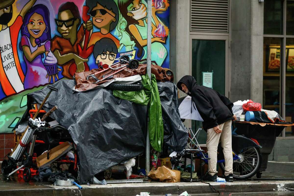 A homeless man looks under a tarp during a rainstorm on Sixth Street in San Francisco.
