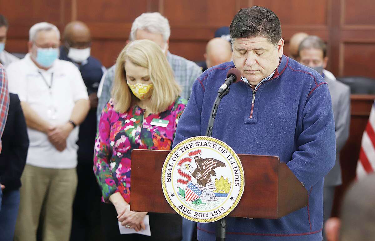 John Badman|The Telegraph Gov. Governor J.B. Pritzker, right, leads a people in a moment of prayer for the six Amazon employees who lost their lives at the Edwardsville facility Friday night. Pritzker, who had been in Edwardsville Saturday, returned Monday to address the storm deaths.
